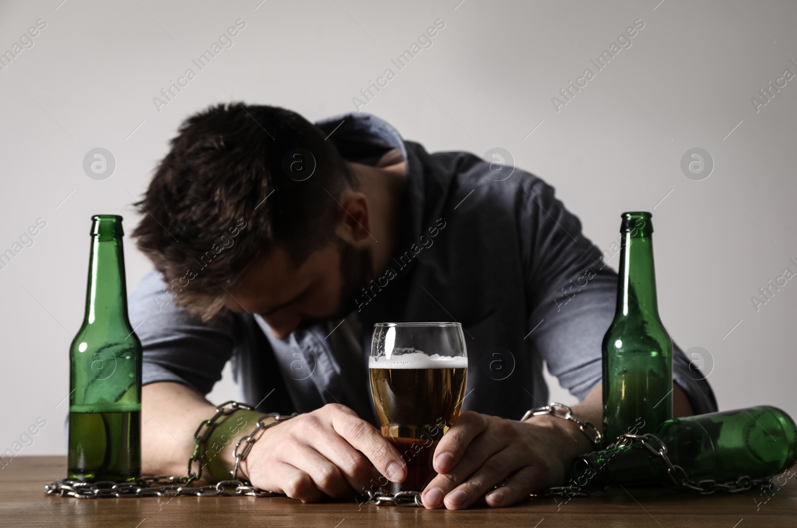 Photo of Addicted man chained to glass of alcoholic drink at wooden table