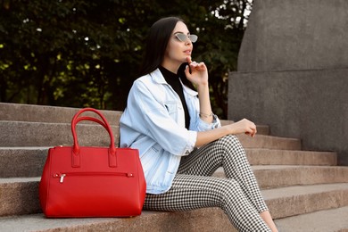 Photo of Young woman with stylish bag sitting on stairs outdoors