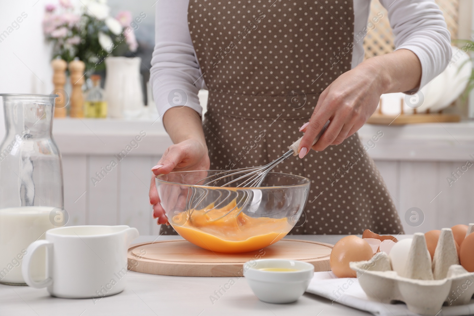 Photo of Woman whisking eggs in bowl at table indoors, closeup