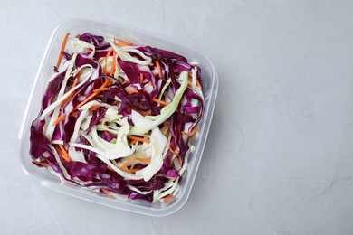 Fresh cabbage salad with shredded carrot in plastic container on light table, top view. Space for text