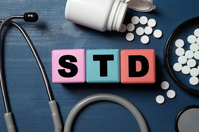 Photo of Wooden cubes with letters STD, pills and stethoscope  on blue table, flat lay