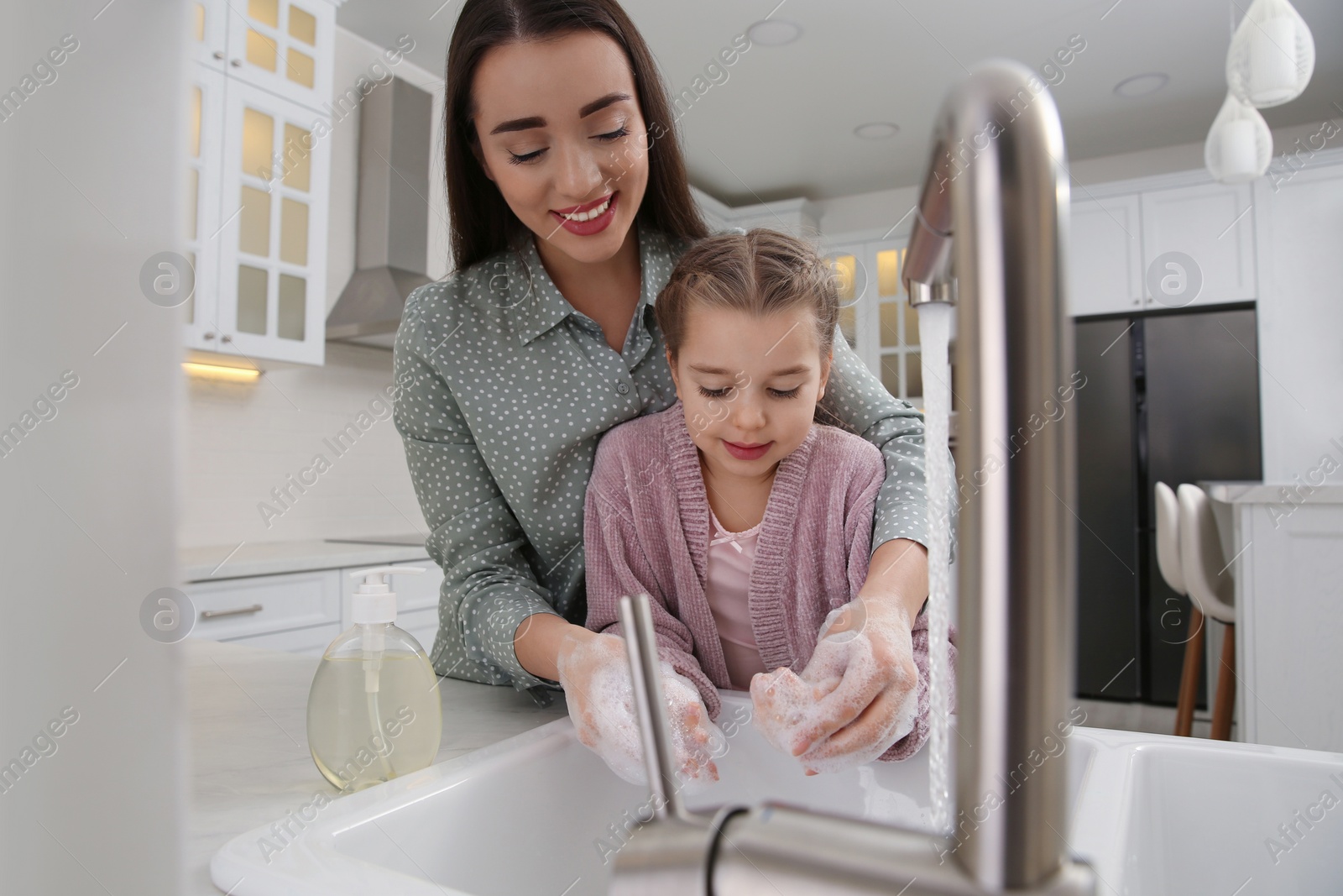 Photo of Mother and daughter washing hands with liquid soap together in kitchen