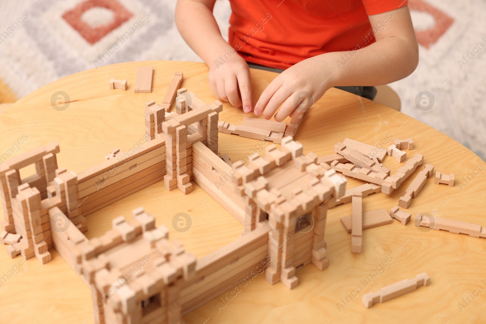 Photo of Little boy playing with wooden construction set at table in room, closeup. Child's toy