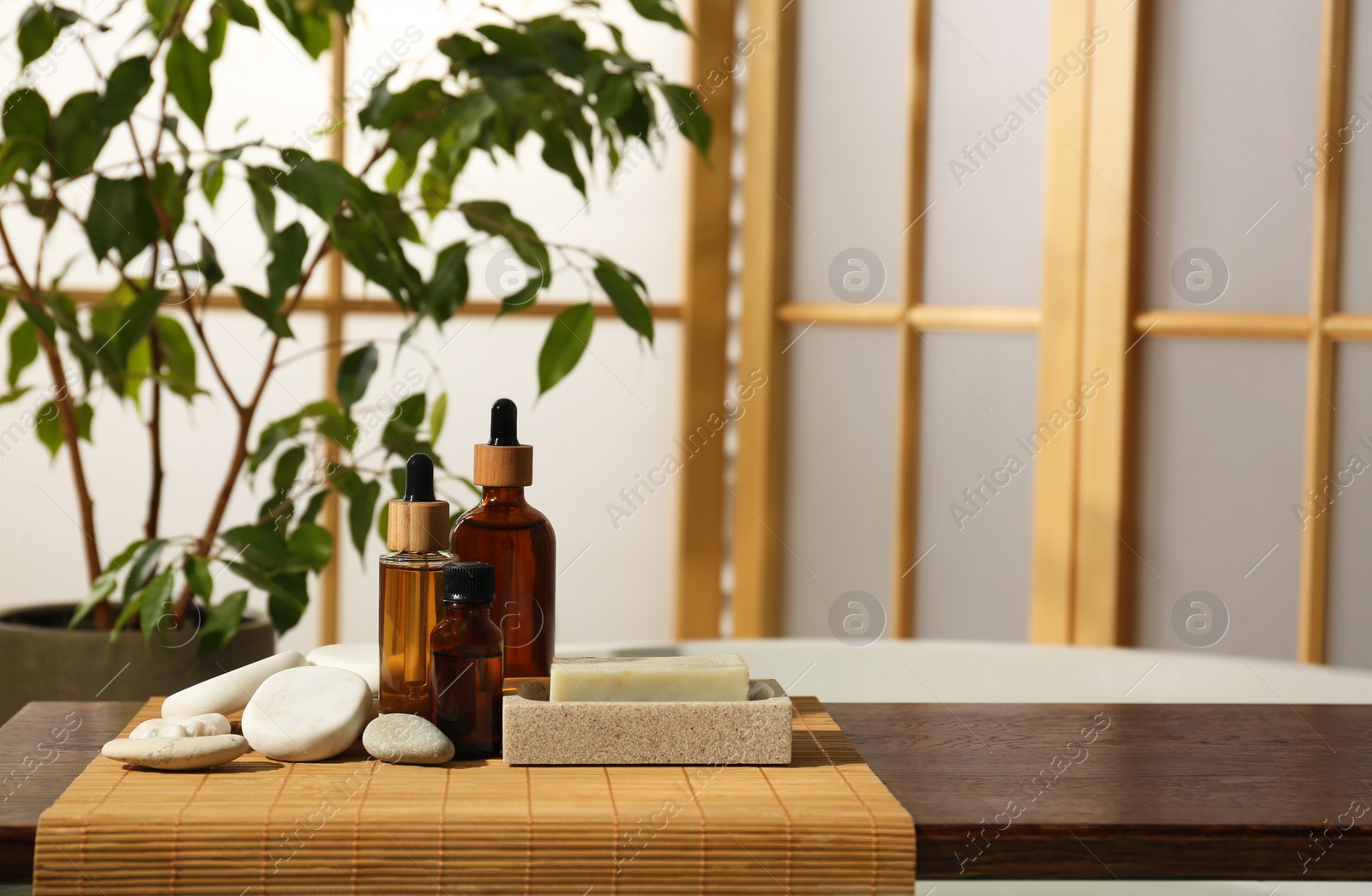 Photo of Wooden tray with spa products and stones on bath tub in bathroom. Space for text