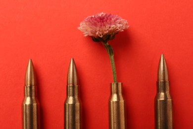 Photo of Bullets and cartridge case with beautiful flower on red background, flat lay