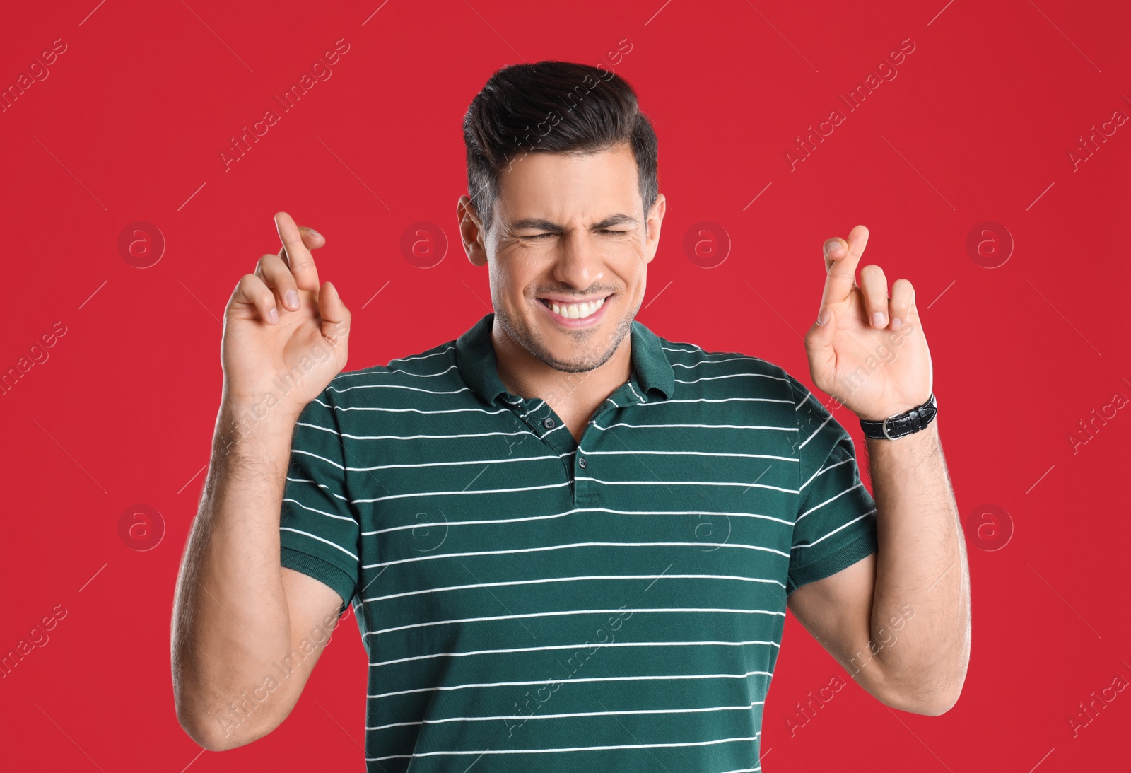 Photo of Man with crossed fingers on red background. Superstition concept