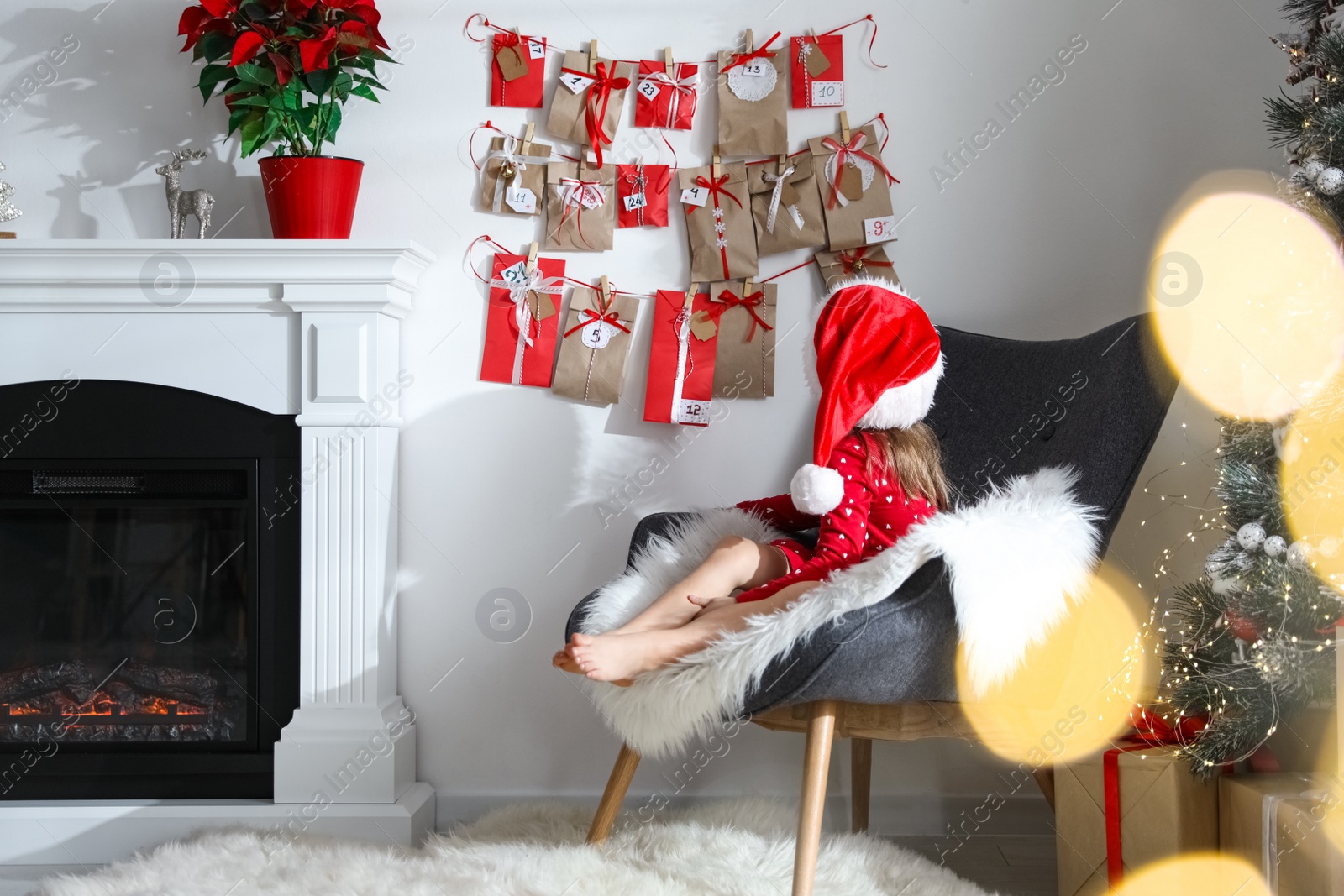 Photo of Cute little girl in Santa hat near Christmas advent calendar at home