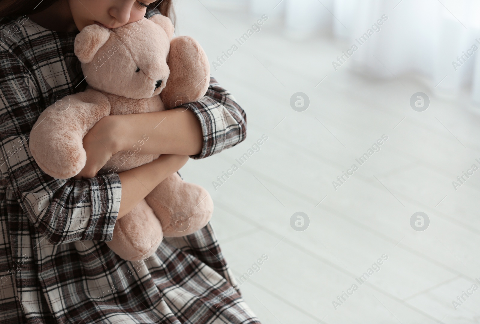 Photo of Upset girl with toy indoors, closeup. Space for text