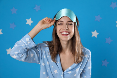 Beautiful woman wearing pajamas and sleep mask on light blue background. Bedtime