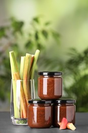 Photo of Jars of tasty rhubarb jam and stalks on grey table