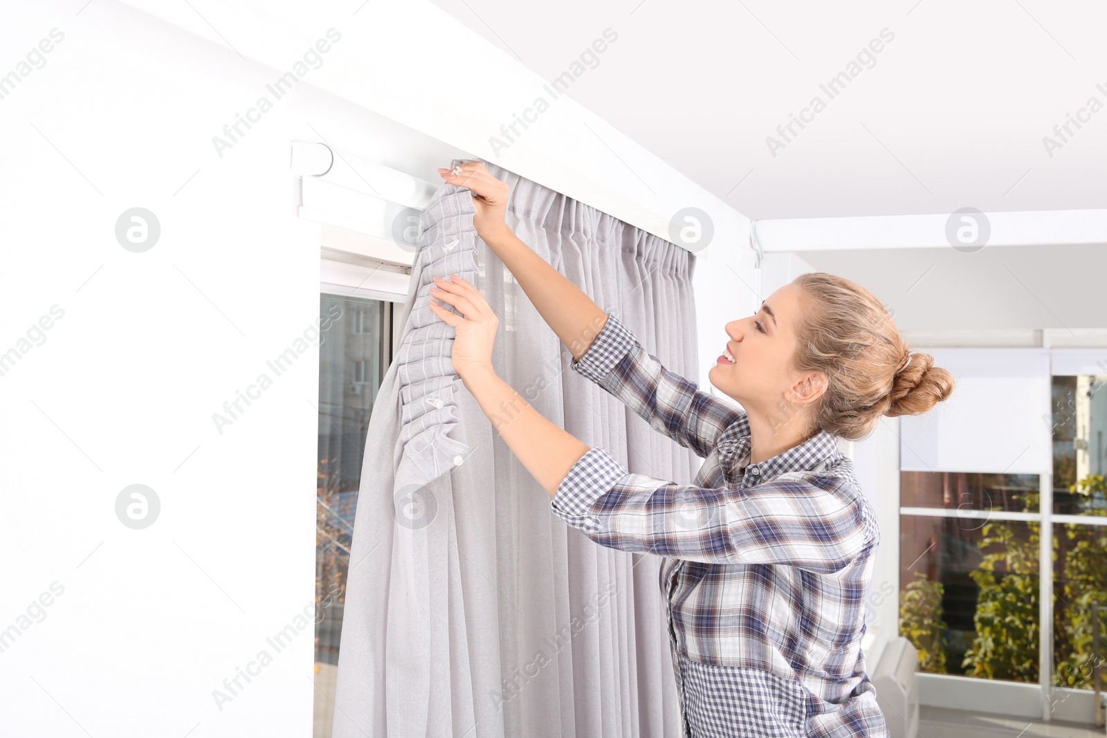 Photo of Woman hanging window curtain indoors. Interior decor element