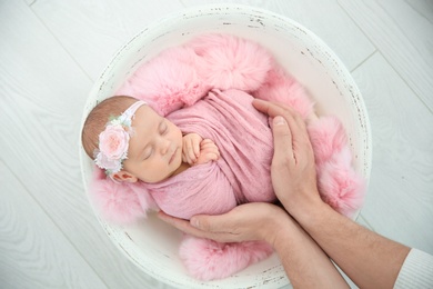 Cute newborn baby girl with her father on light background, top view