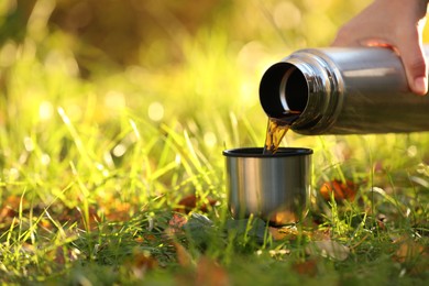 Photo of Woman pouring tea from thermos into cup lid on green grass outdoors, closeup. Space for text