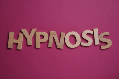 Photo of Word HYPNOSIS made with wooden letters on magenta background, flat lay