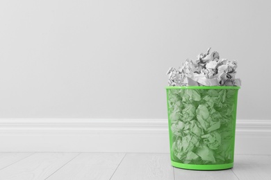 Photo of Metal bin and crumpled paper against light wall, space for text