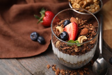 Photo of Tasty granola with berries, nuts and yogurt in glass on wooden table, closeup. Space for text