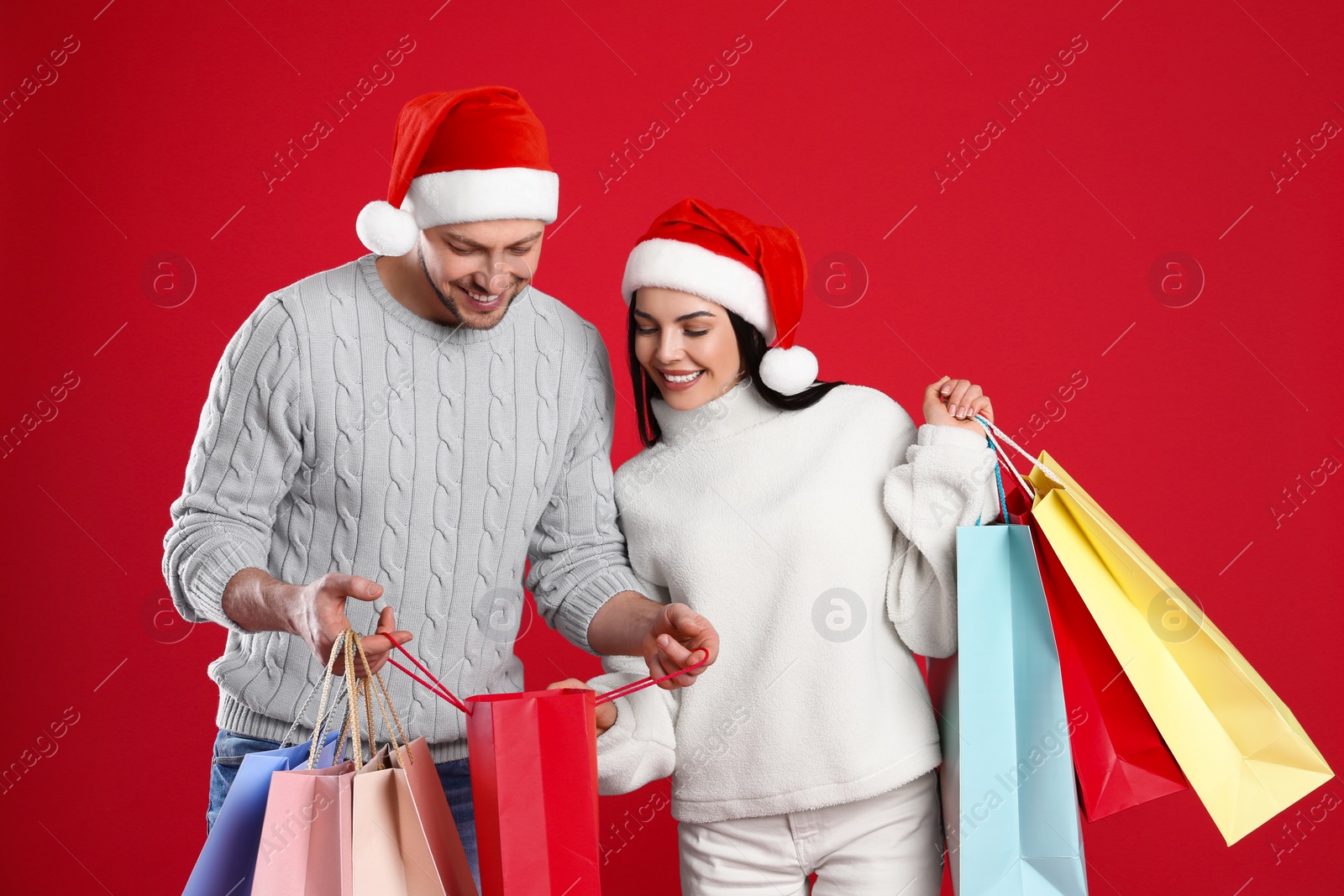 Photo of Happy couple with paper bags on red background. Christmas shopping