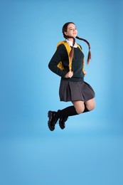 Photo of Teenage girl in school uniform with backpack jumping on light blue background