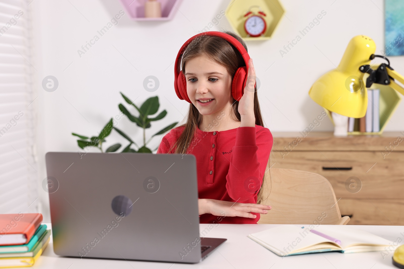 Photo of E-learning. Cute girl raising her hand to answer during online lesson at table indoors