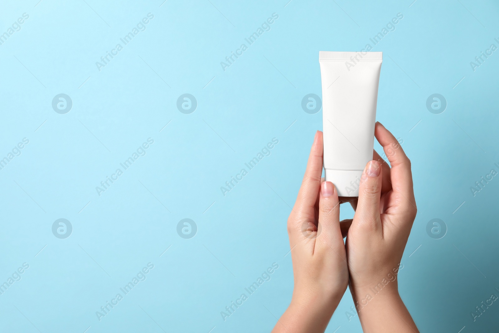 Photo of Woman with tube of hand cream on light blue background, closeup. Space for text