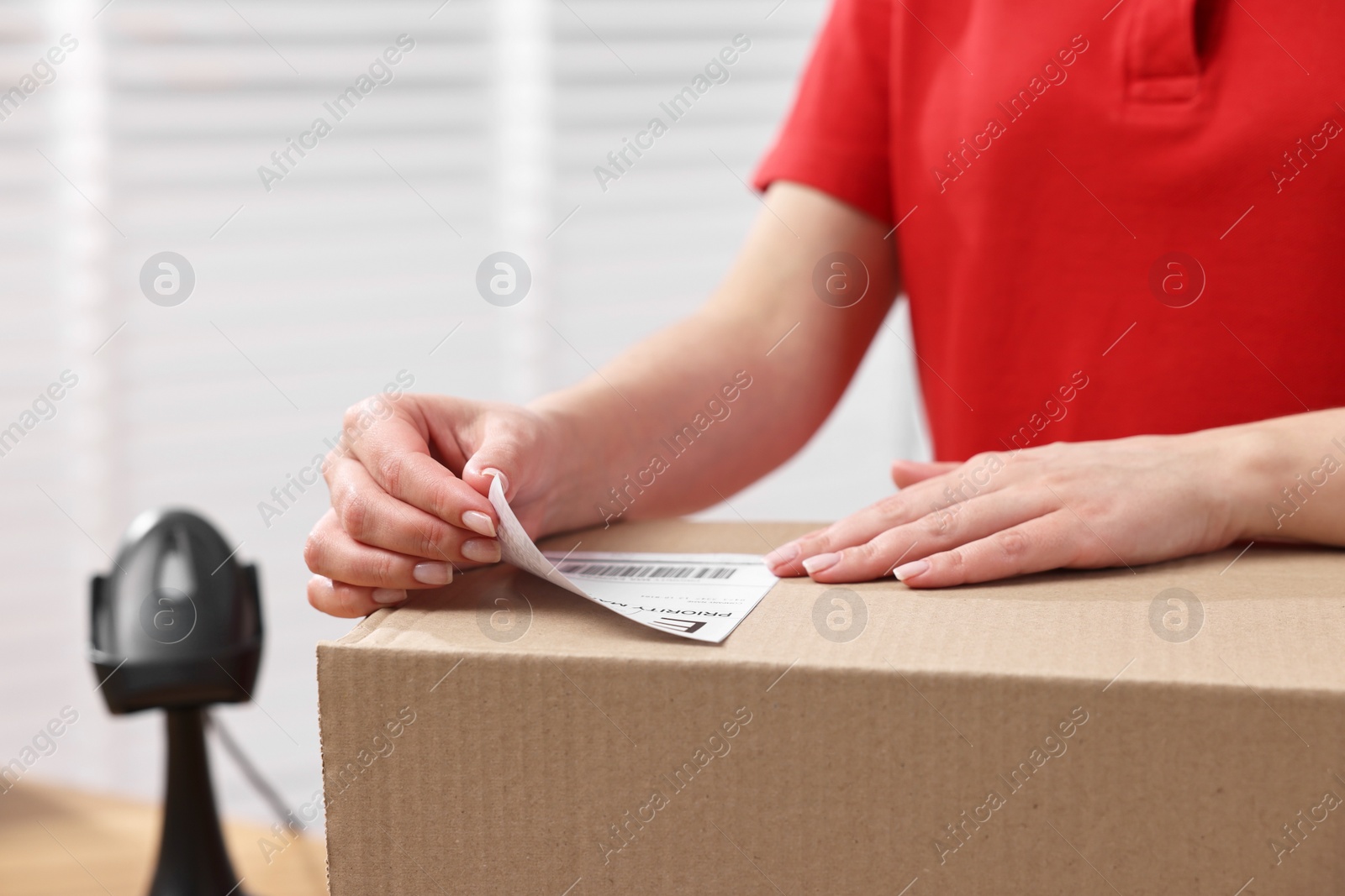 Photo of Parcel packing. Post office worker sticking barcode on box indoors, closeup