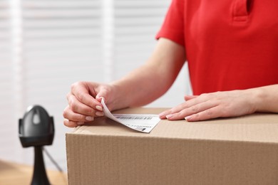 Photo of Parcel packing. Post office worker sticking barcode on box indoors, closeup