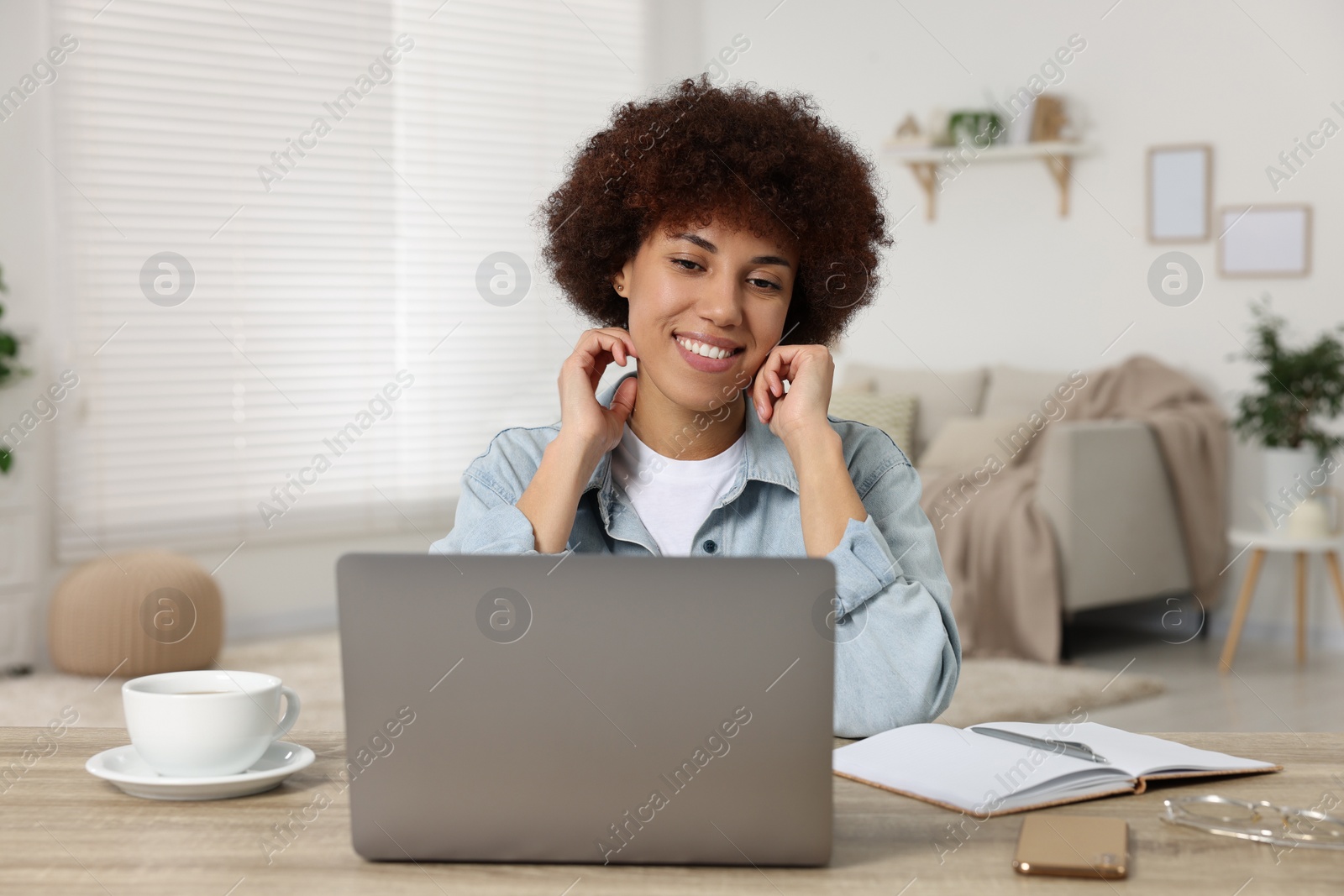 Photo of Young woman using laptop at wooden desk in room