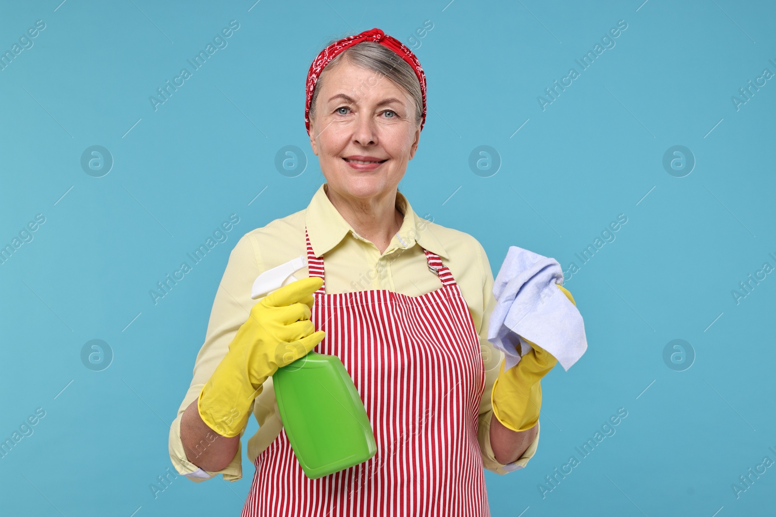 Photo of Happy housewife with spray bottle and rag on light blue background