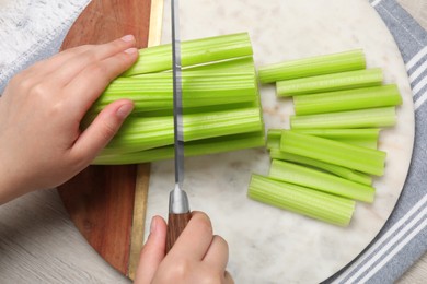 Photo of Woman cutting fresh green celery at white table, top view