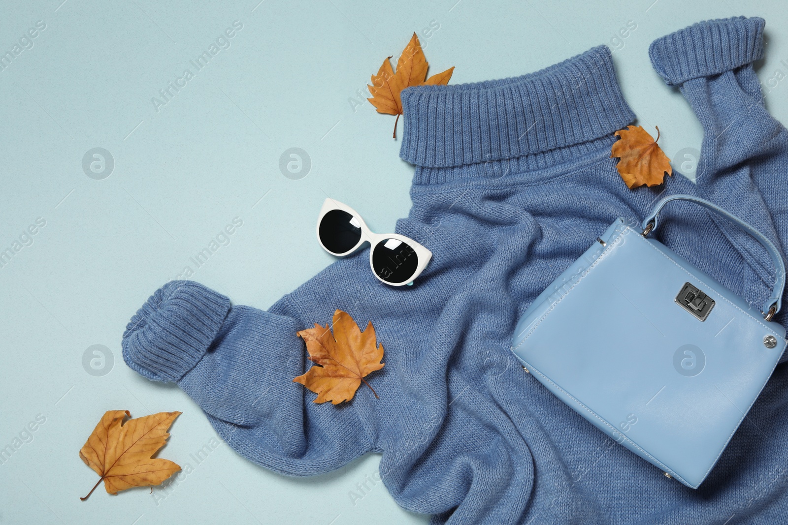 Photo of Flat lay composition with sweater and dry leaves on light blue background. Autumn season