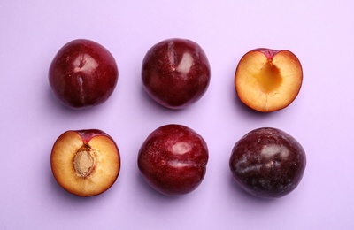 Photo of Delicious ripe plums on violet background, flat lay
