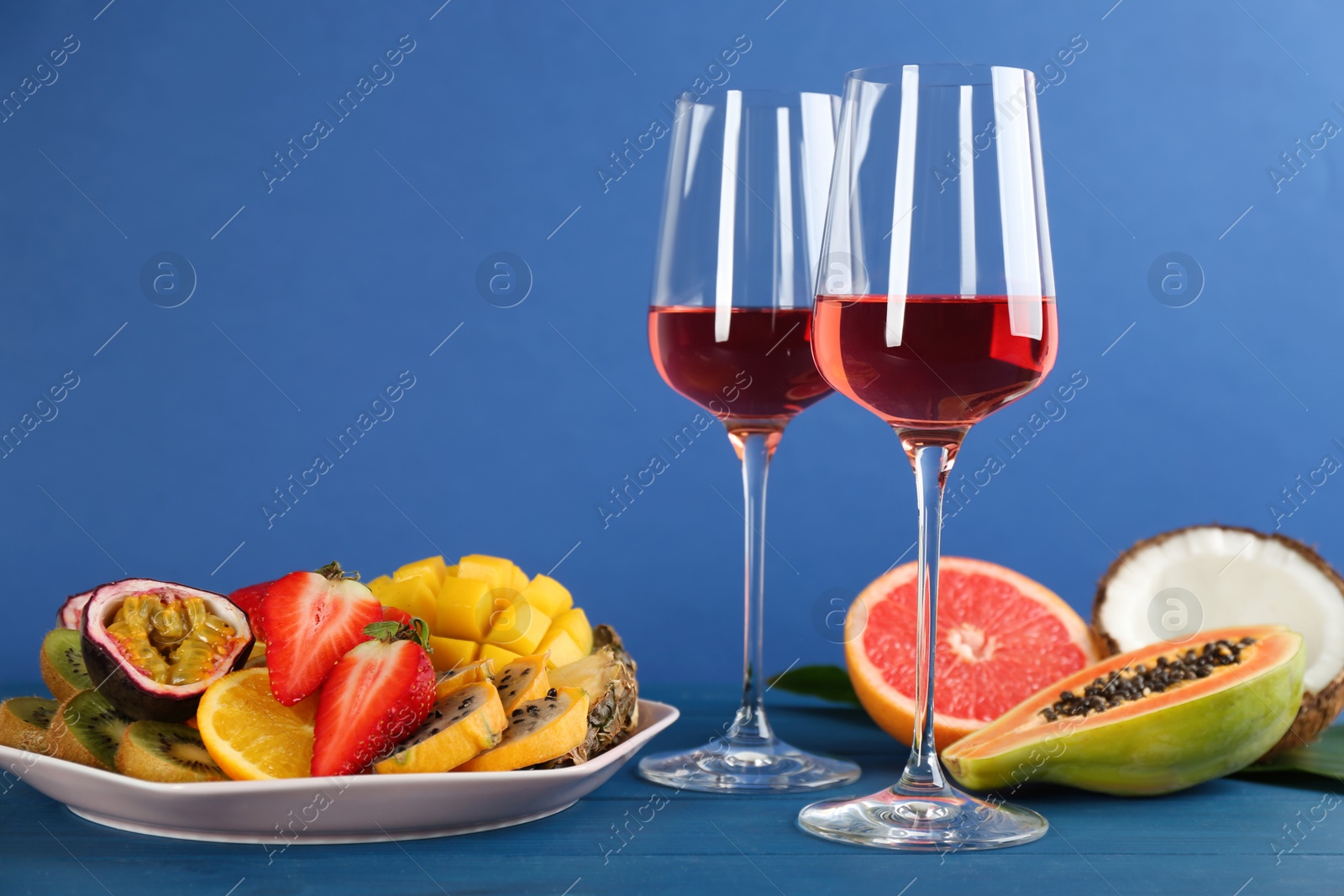 Photo of Delicious exotic fruits and glasses of wine on blue wooden table