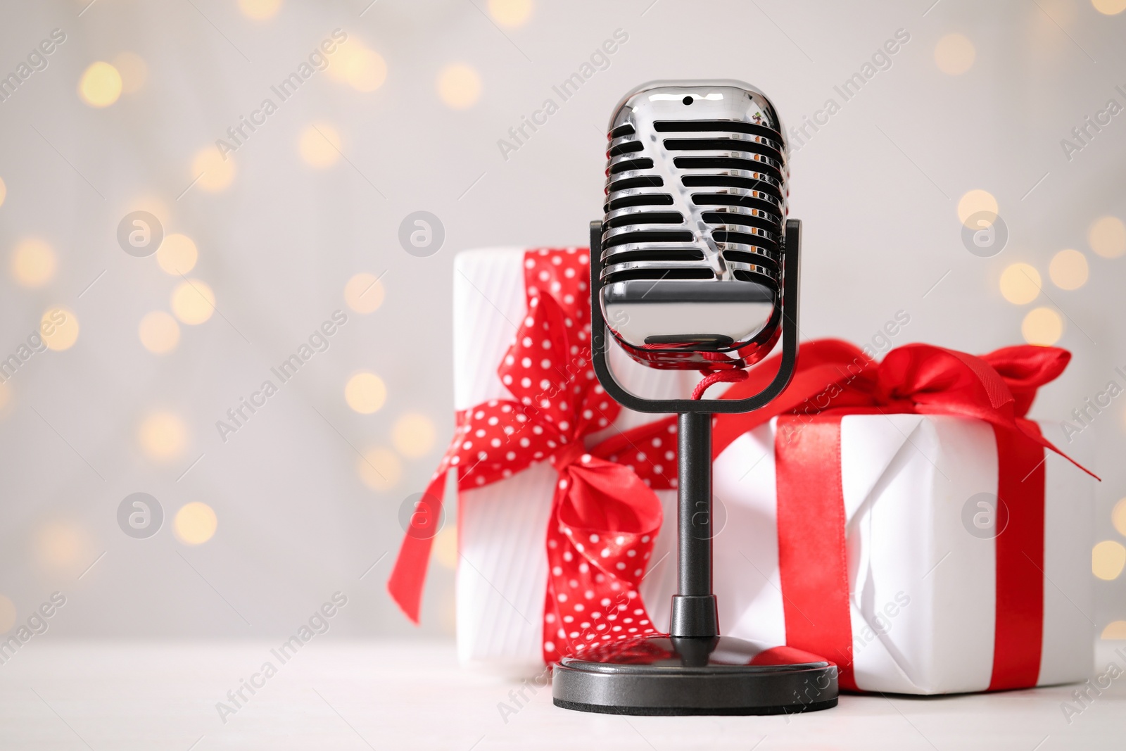Photo of Retro microphone and gift boxes on table against blurred lights, space for text. Christmas music