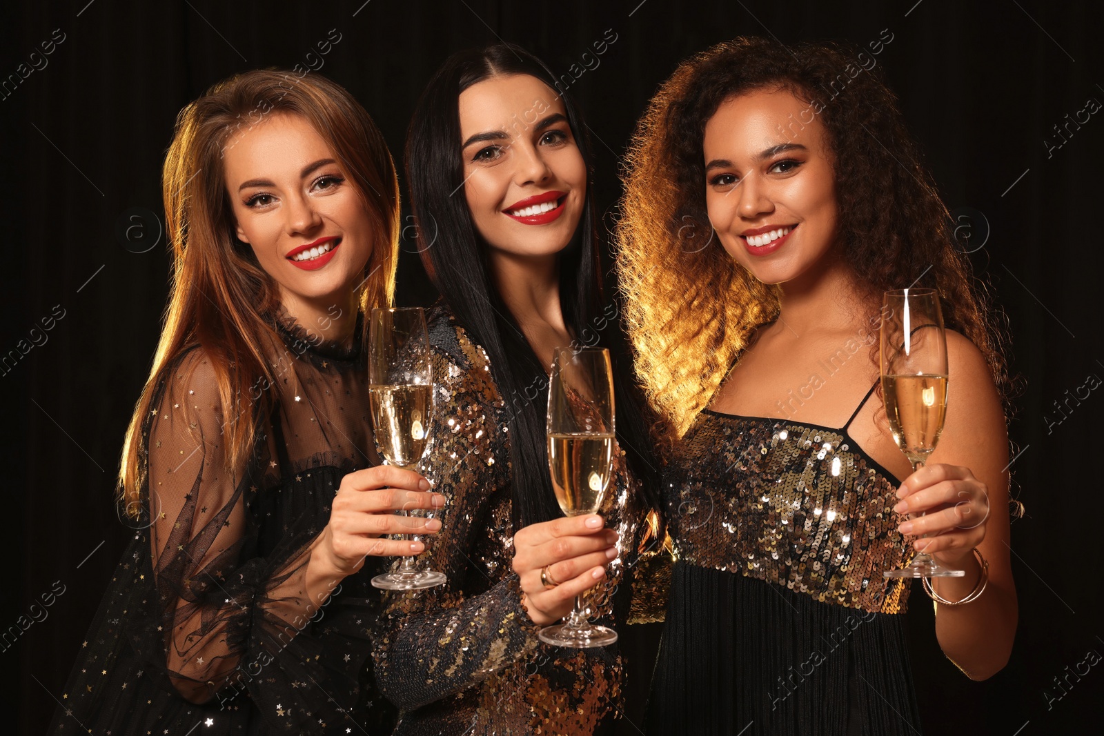 Photo of Happy women with glasses of sparkling wine celebrating New Year on black background