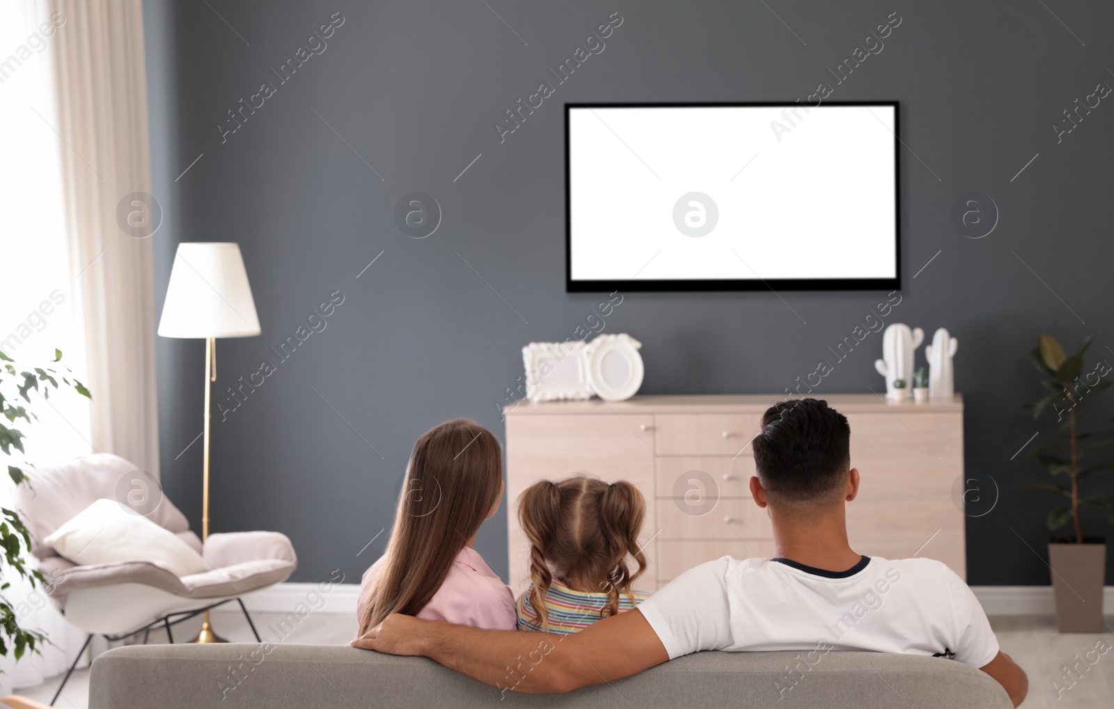 Photo of Family watching TV on sofa at home, back view