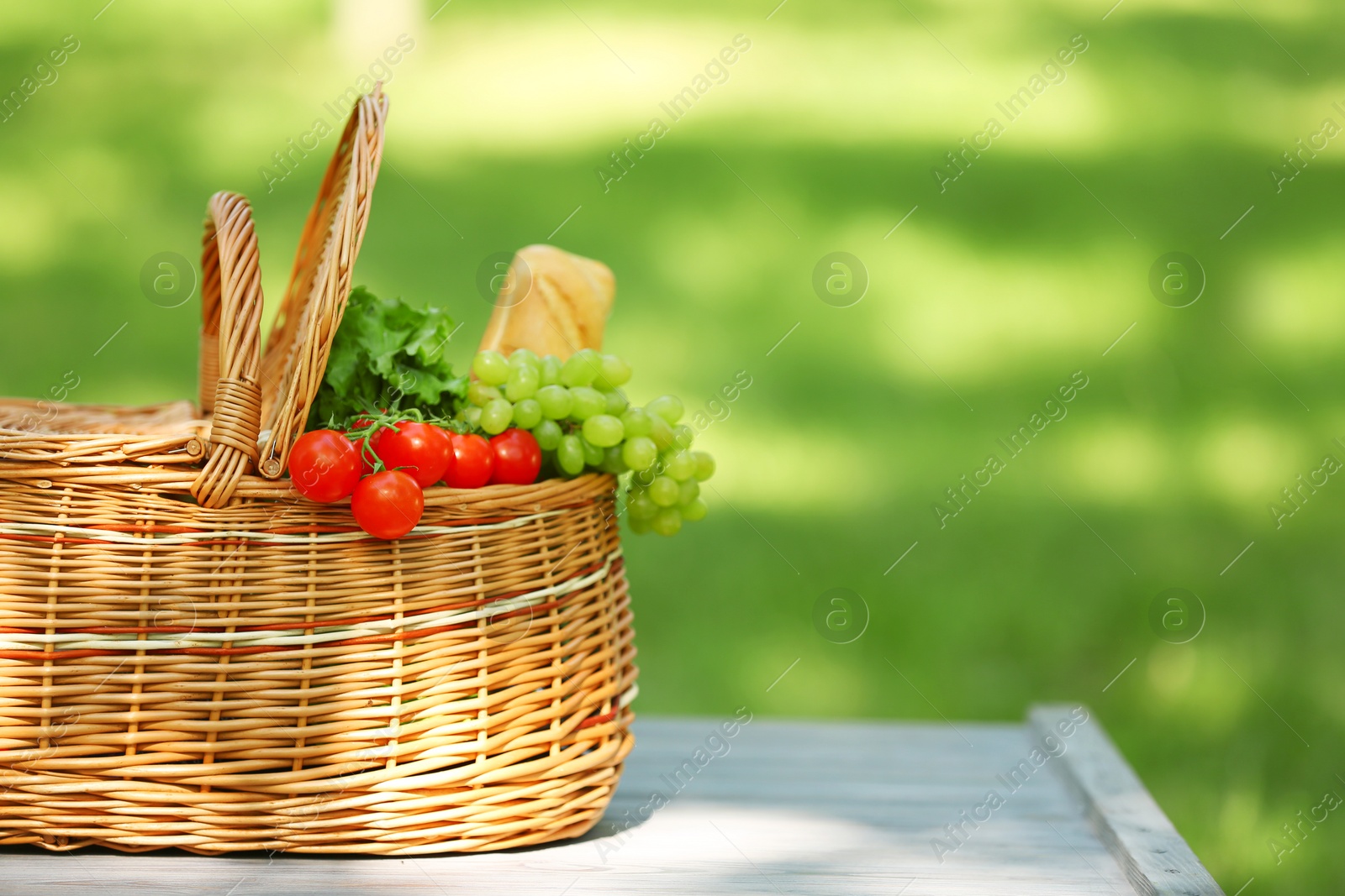 Photo of Wicker basket with food on table in park, space for text. Summer picnic