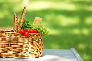 Photo of Wicker basket with food on table in park, space for text. Summer picnic