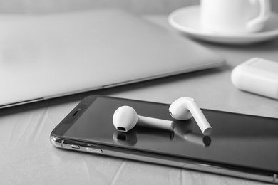 Photo of Modern wireless earphones and mobile phone on light grey stone table