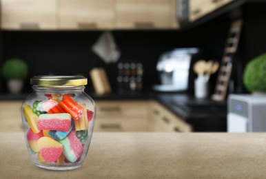 Image of Glass jar with tasty gummy candies on light brown table in kitchen. Space for text