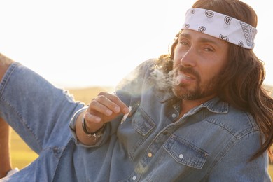 Photo of Hippie man in headband smoking joint outdoors