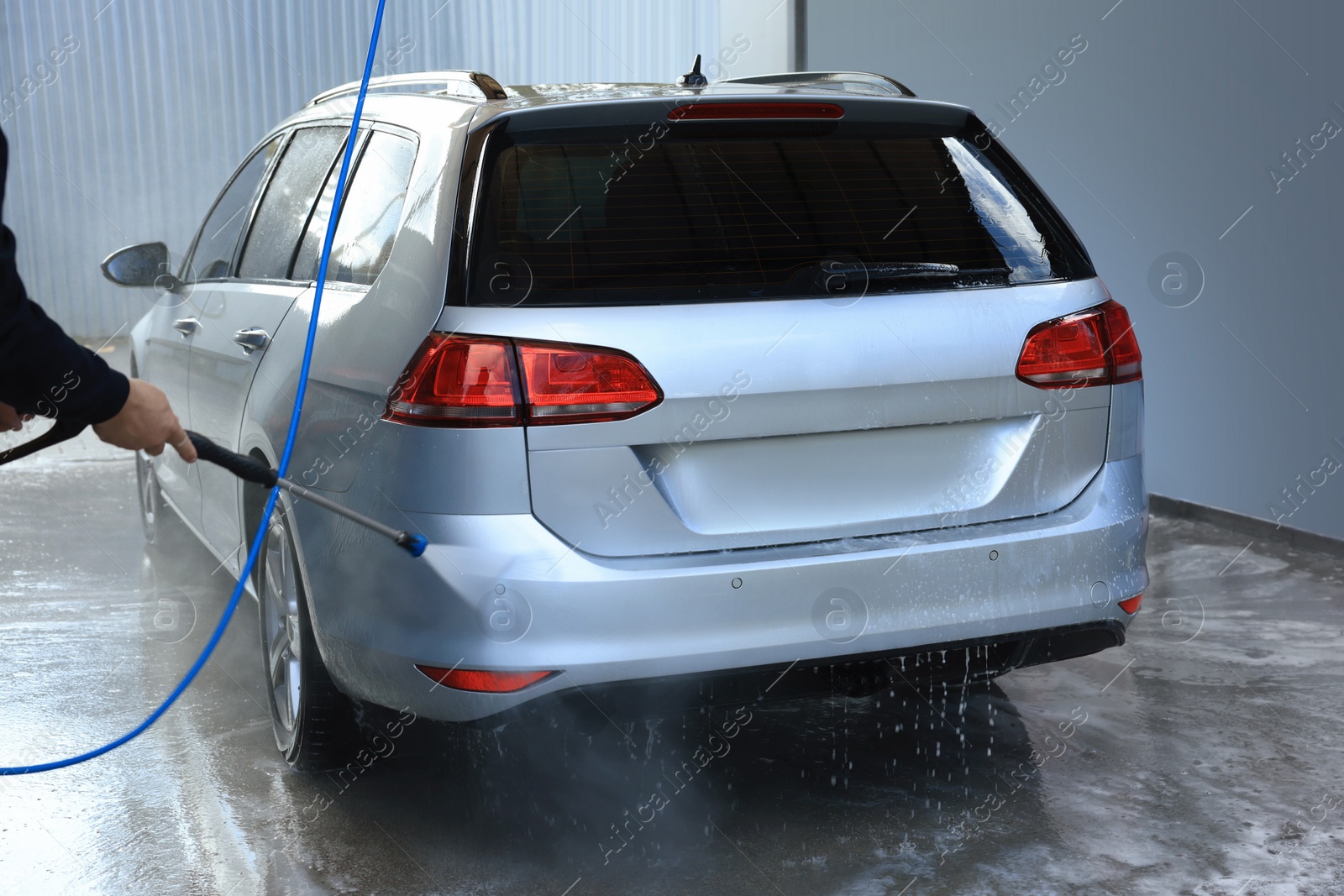 Photo of Man washing auto with high pressure water jet at outdoor car wash, closeup