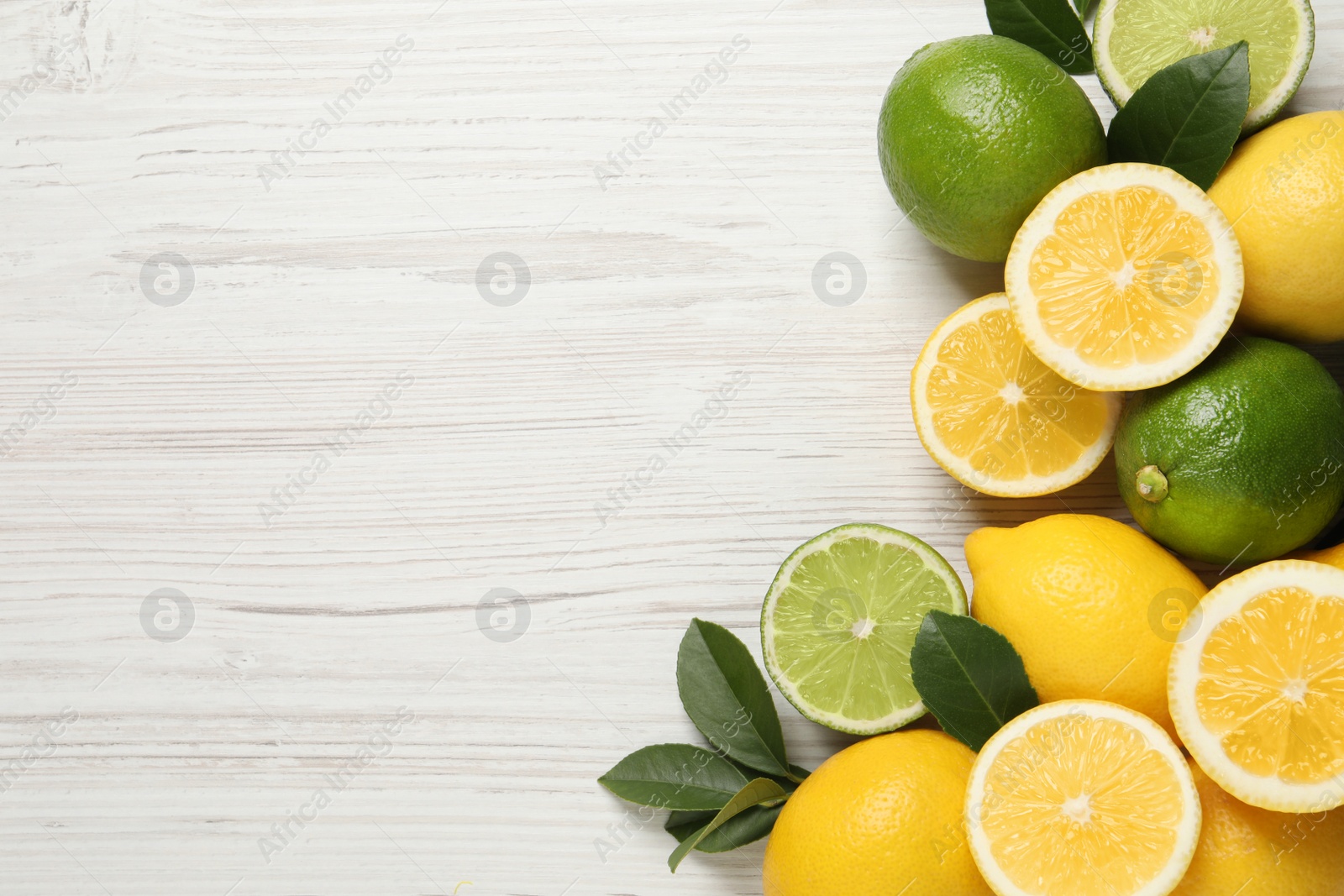 Photo of Fresh ripe lemons, limes and green leaves on white wooden background, flat lay. Space for text