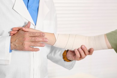 Orthopedist applying bandage onto patient's elbow in clinic, closeup