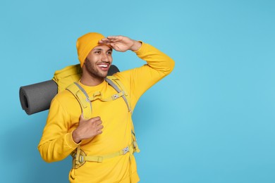 Photo of Happy tourist with backpack on light blue background, space for text