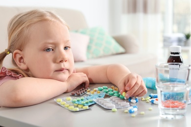 Photo of Little child with many different pills at table indoors. Danger of medicament intoxication