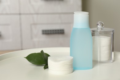 Photo of Cotton pads, leaves and makeup removal product on white table in bathroom. Space for text