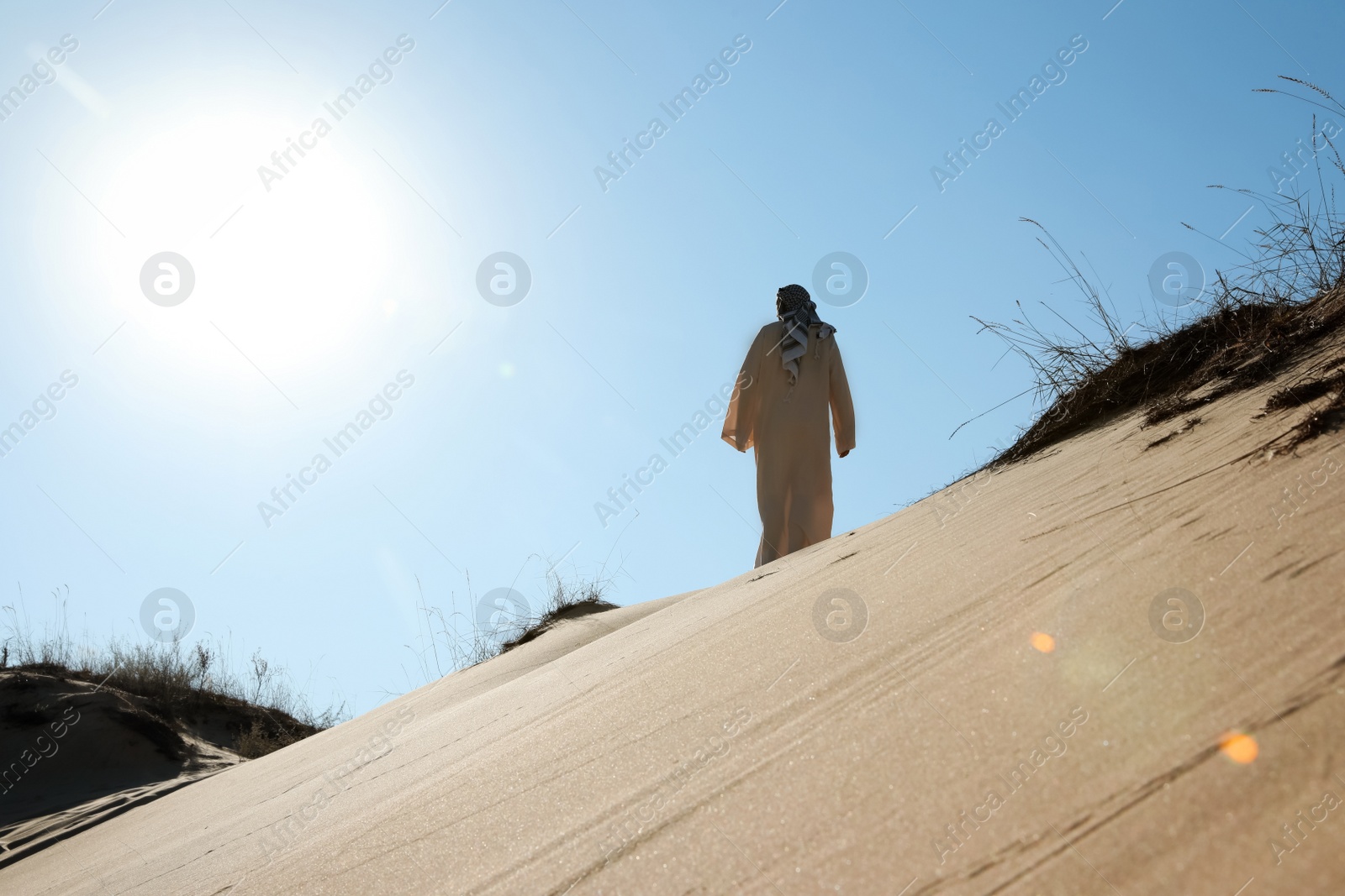 Photo of Man in arabic clothes walking through desert on sunny day, back view