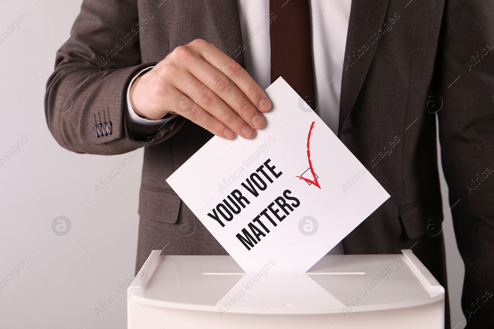 Image of Man putting paper with text Your Vote Matters and tick into ballot box on light grey background