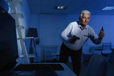 Professional security guard with portable radio set and gun in dark office