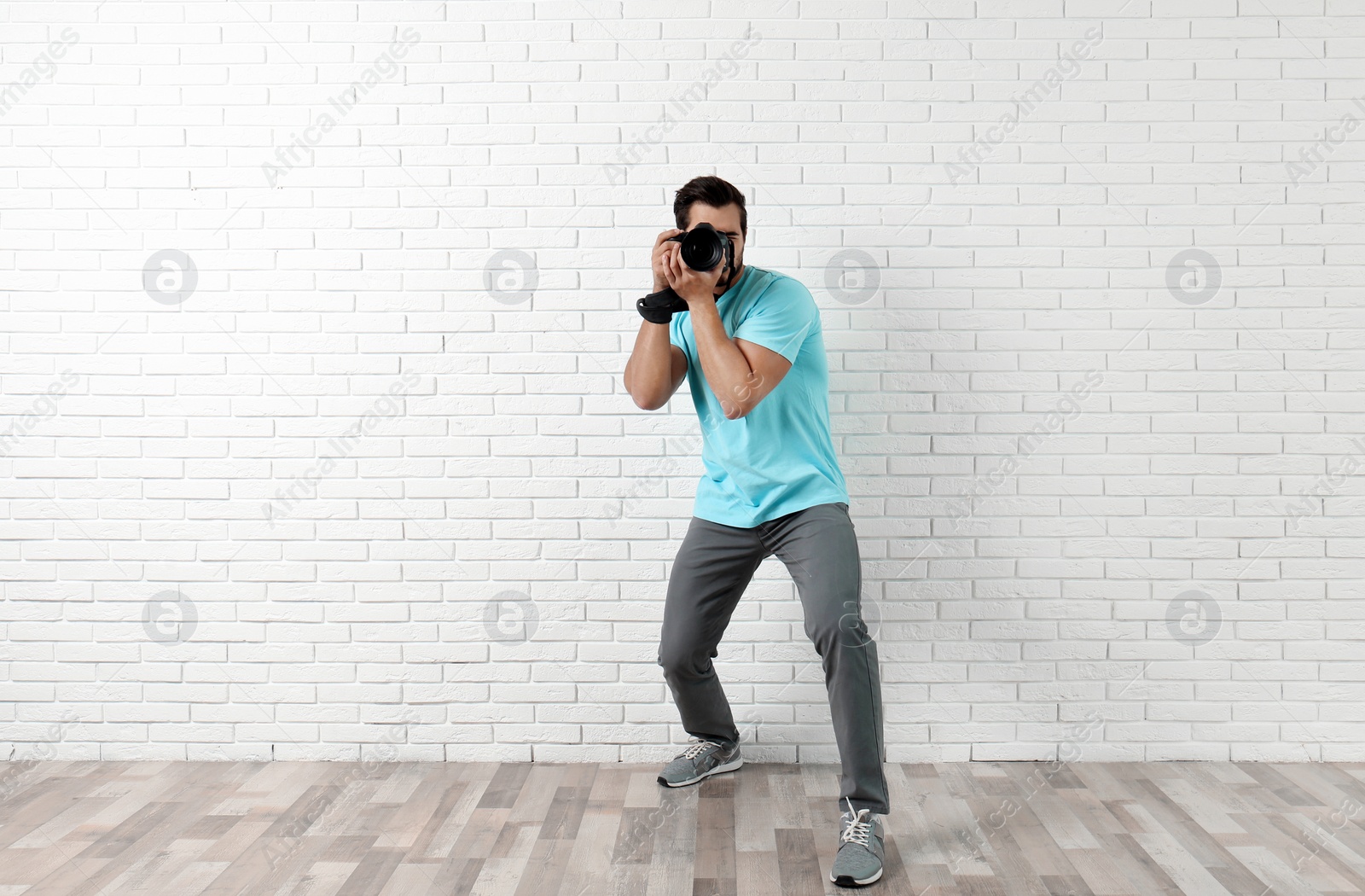 Photo of Young professional photographer taking picture near brick wall. Space for text